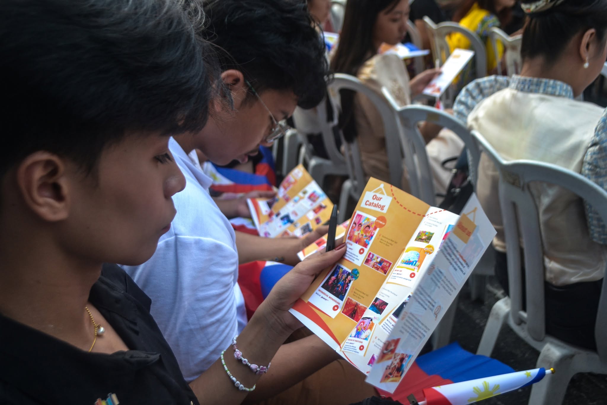 Attendees seated at an event reading folded TicketwavePH catalogue leaflets